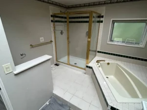 Dated 1990s master bathroom before remodel — old tile shower with brass frame and built-in tub
