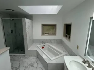 Modern remodeled master bathroom with frameless glass walk-in shower, marble tub deck and natural skylight