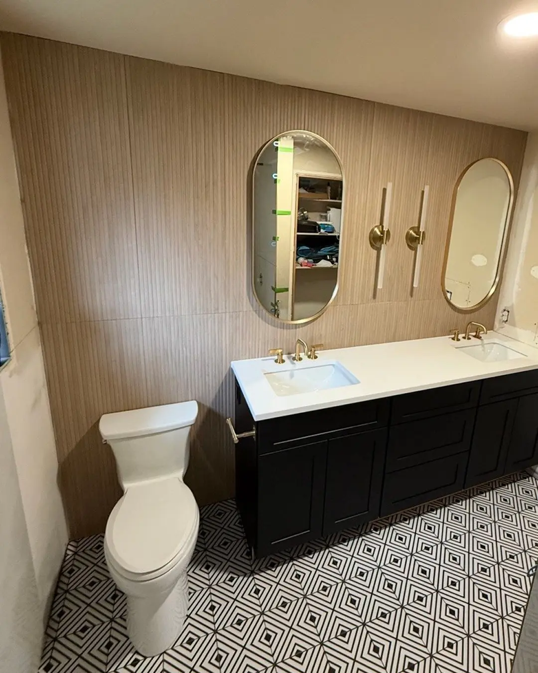 Fully renovated bathroom with black double vanity, gold fixtures and black-and-white geometric floor tile