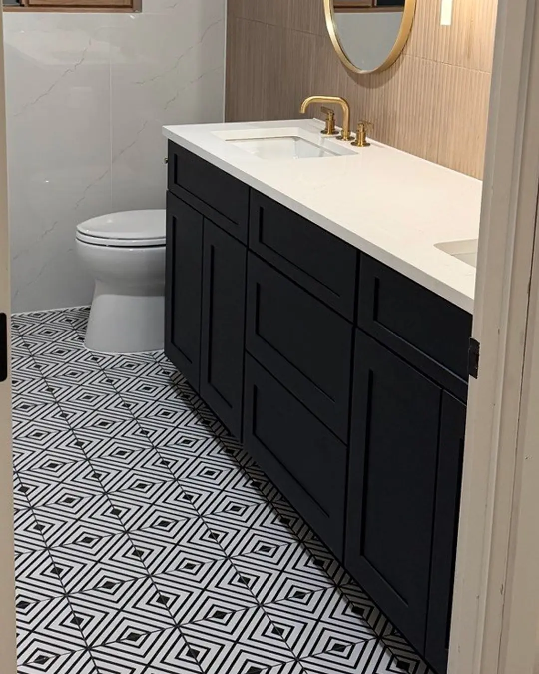 Modern black shaker vanity with quartz top, gold faucet and diamond-pattern floor tile in renovated bathroom
